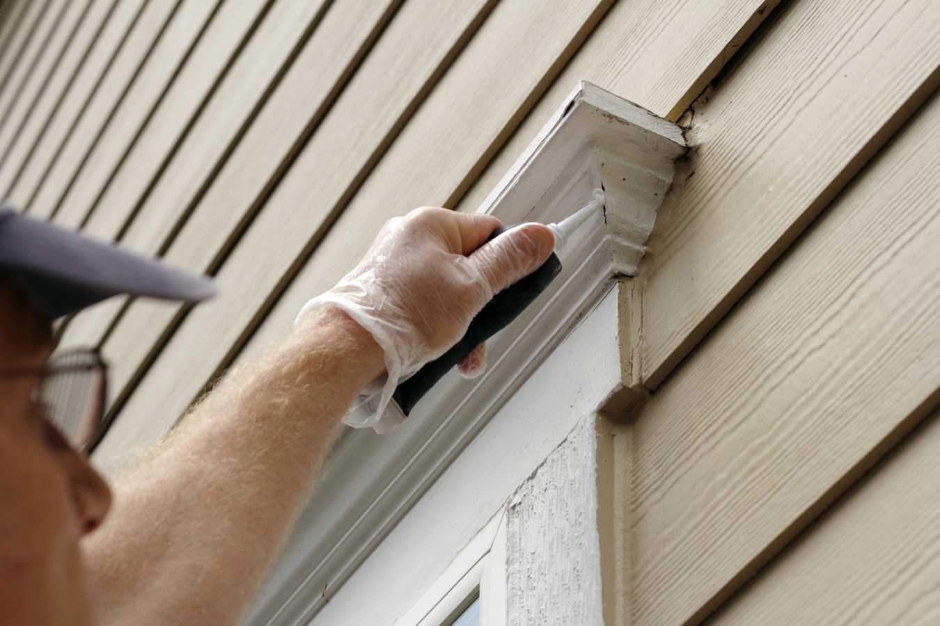 Man outdoors filling holes that developed around an exterior wood repair los angeles home window frame.